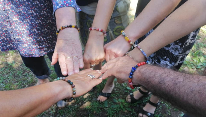 Gros plan sur les bras de 6 personnes qui joignent leurs mains ornées de bracelets.