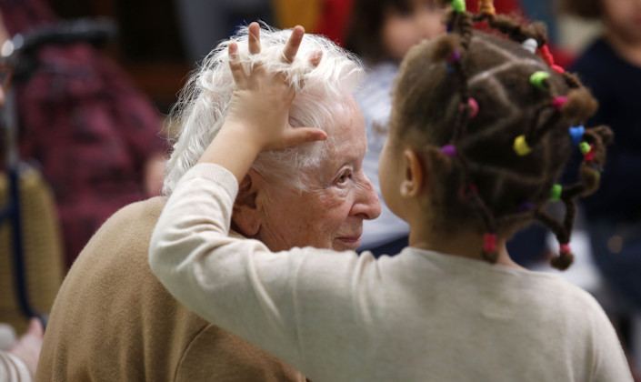 Une petite fille caresse les cheveux blancs d'une dame âgée qui sourit