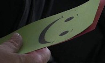 Main tenant un papier jaune sur lequel un smiley souriant est imprimé