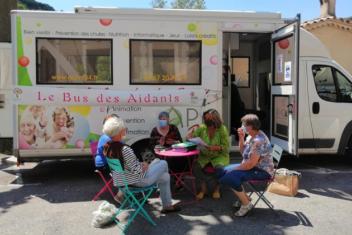 Groupe de quatre personnes assises autour d'une table discutent devant le camping car "Bus des aidants"